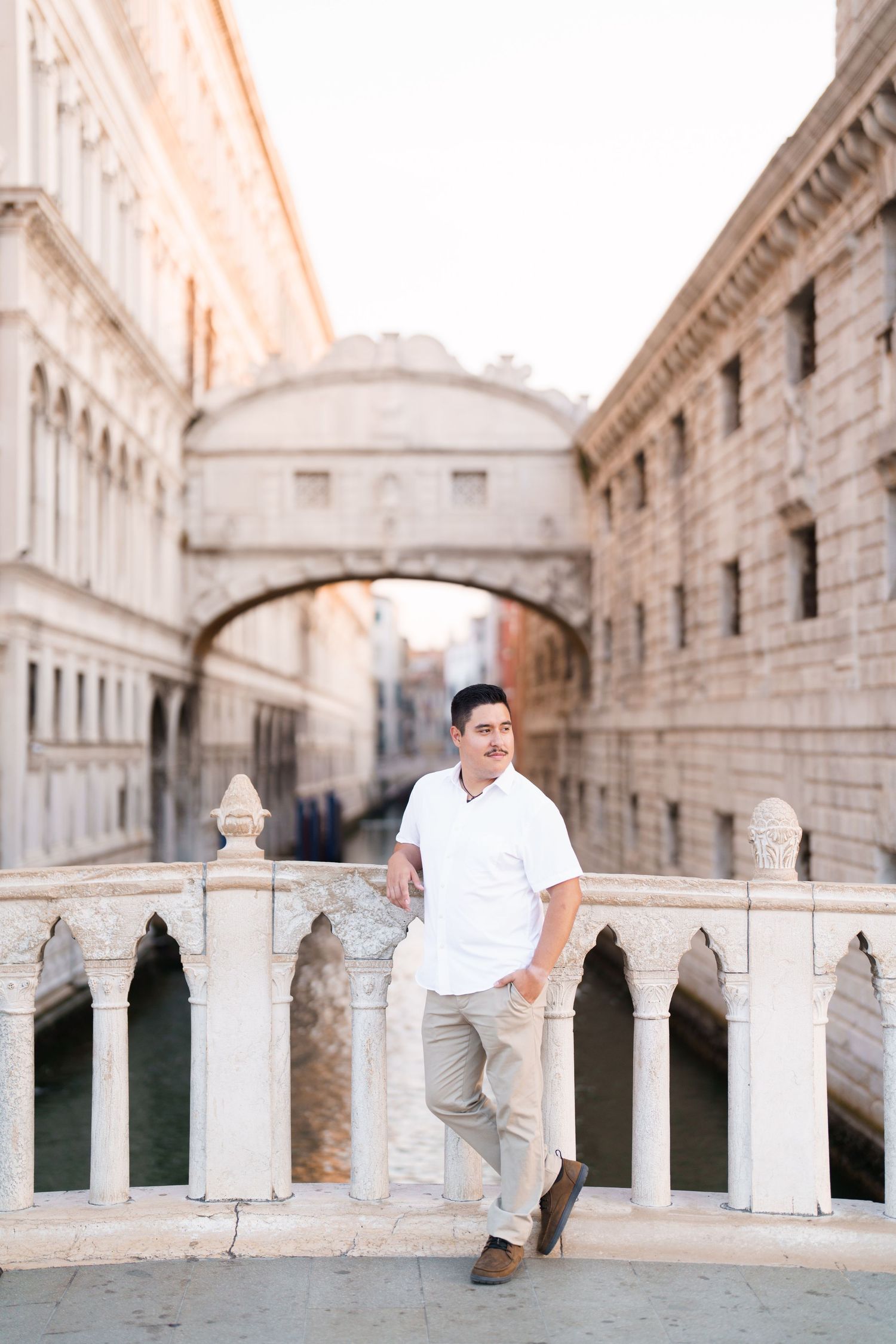 A person in white sits along a stone balustrade of an ornate classical building with arched columns and architecture.