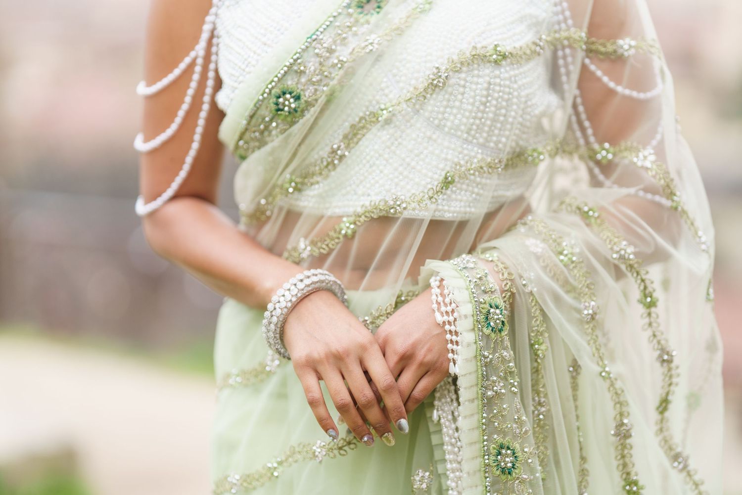 Close-up details of a cream colored saree with delicate embroidery and pearl embellishments.
