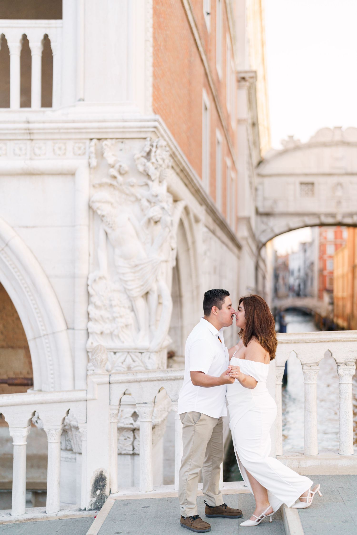 A couple shares romantic moments along Venice's iconic arched colonnade with ornate architectural details and bridges.