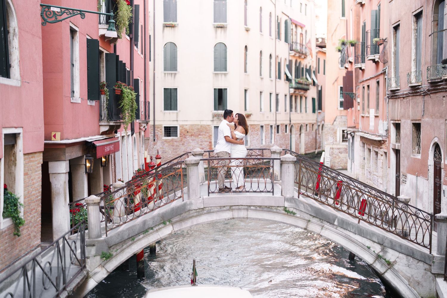 Scenic view of narrow canals with traditional bridges and pink buildings in Venice, Italy during daytime.