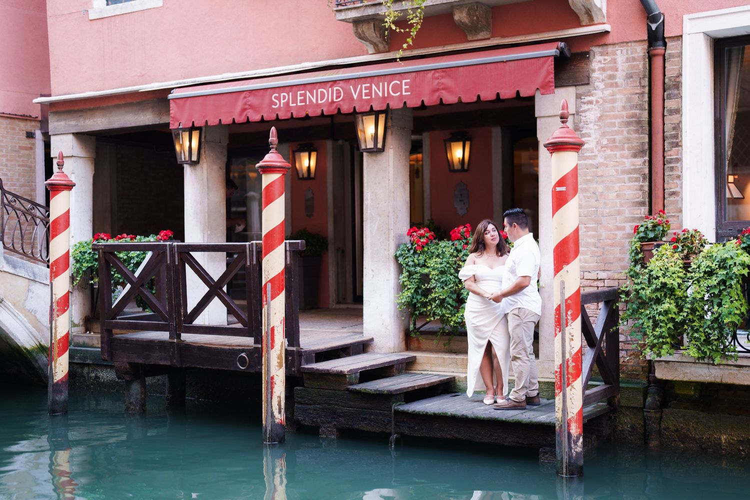 A pink building facade with striped mooring poles and gondolas along a narrow Venice canal waterway.