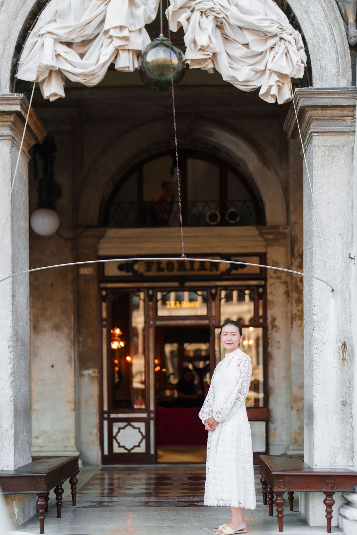 Woman in white dress standing before Caffè Florian historic entrance in Venice, Italy.