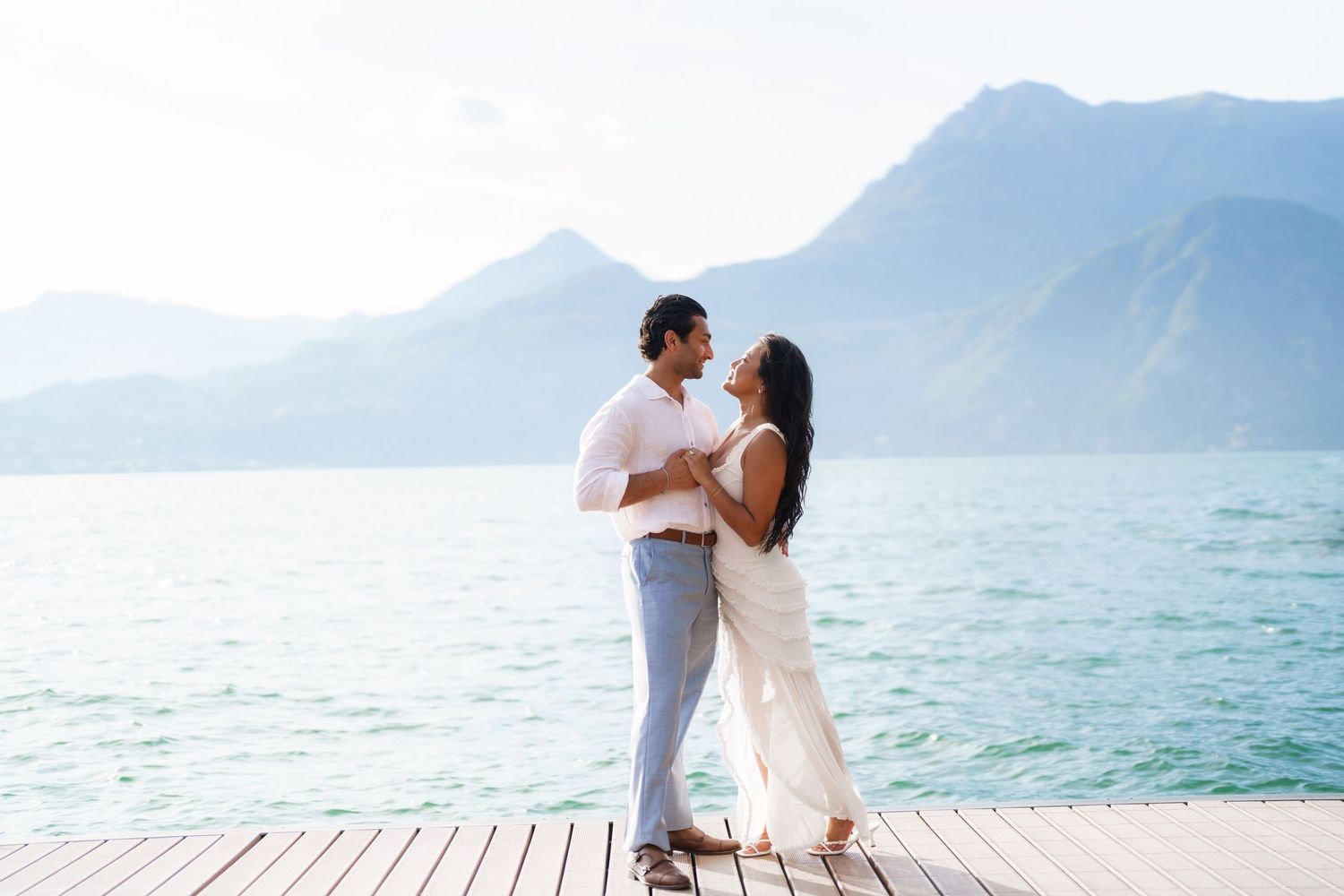 Couple dancing on a wooden dock with turquoise lake and mountain backdrop in a romantic outdoor setting.