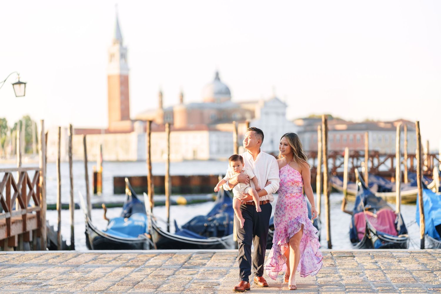 Family strolling along Venice waterfront with gondolas and San Giorgio Maggiore church in background.