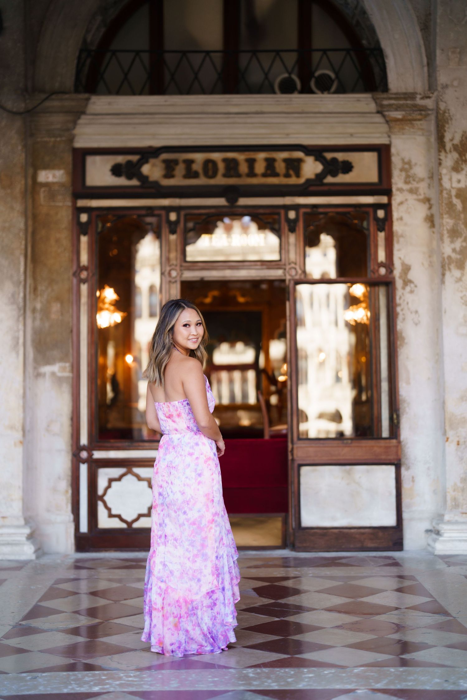 Woman in floral pink maxi dress posing outside Cafe Florian in Venice, Italy.