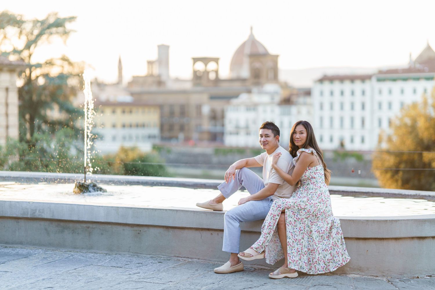 Couple sitting by a fountain with Florence skyline and Duomo in the background during golden hour.