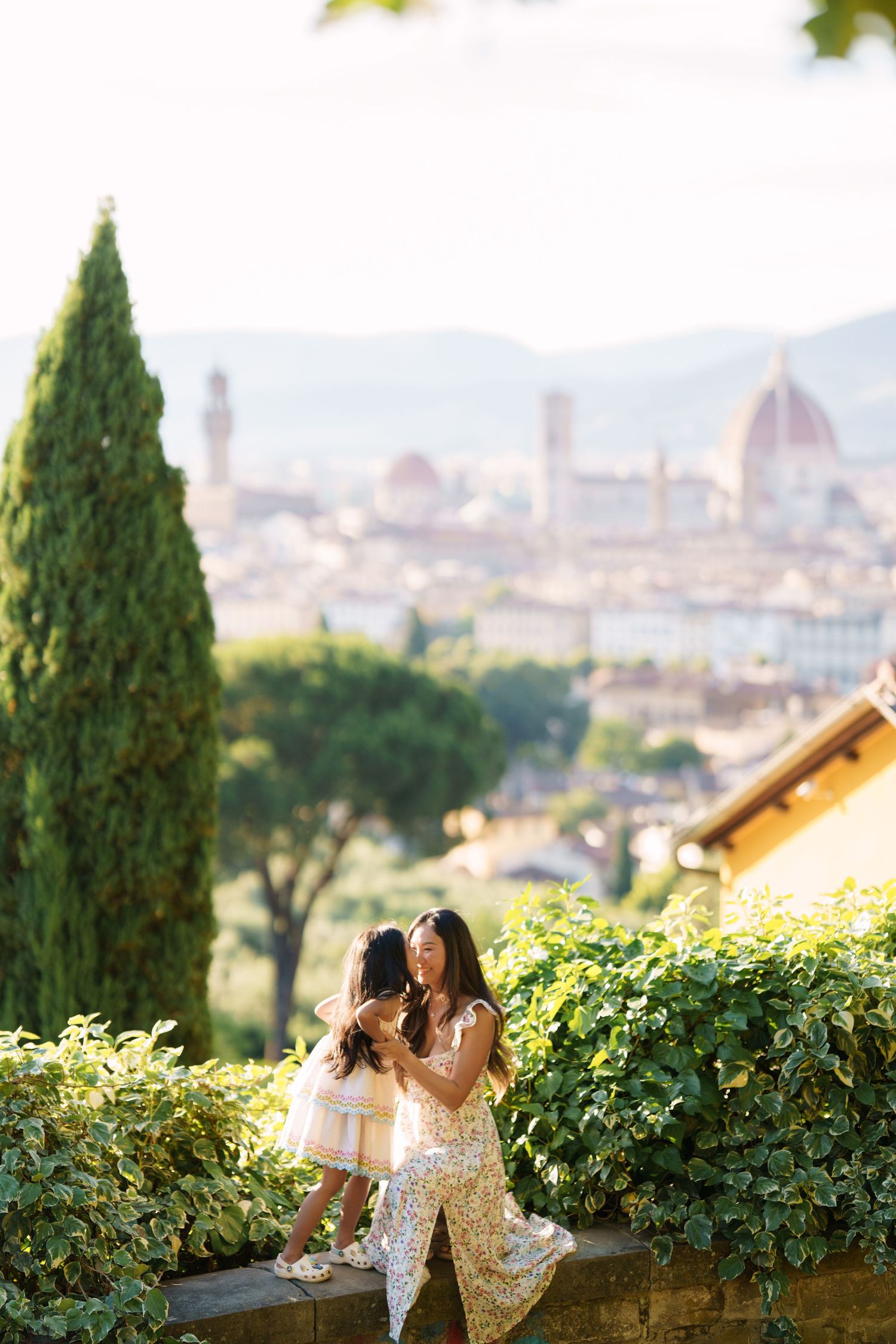 Mother and daughter in matching golden dresses share a tender moment with Florence skyline and cathedral backdrop.