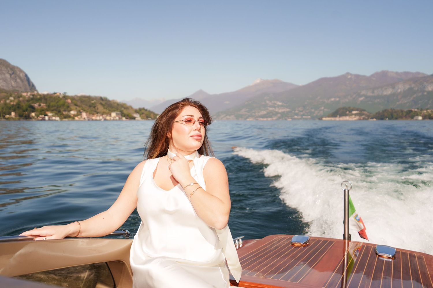 Woman in white dress riding a wooden boat on a scenic mountain lake on a sunny day.