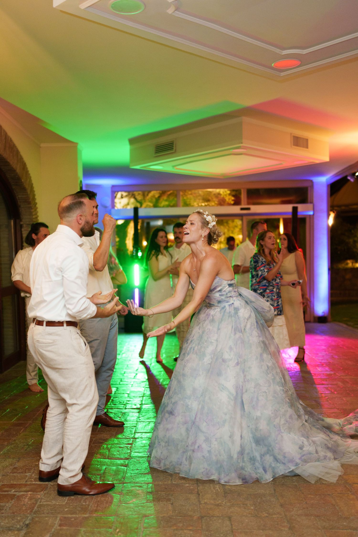 Bride in blue floral gown dances with groom in white shirt at colorful wedding reception.