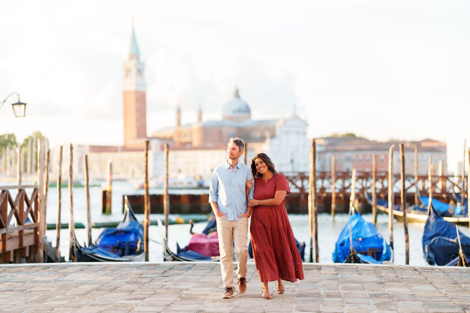 Couple embracing on Venice waterfront with gondolas and San Giorgio Maggiore church in soft morning light.