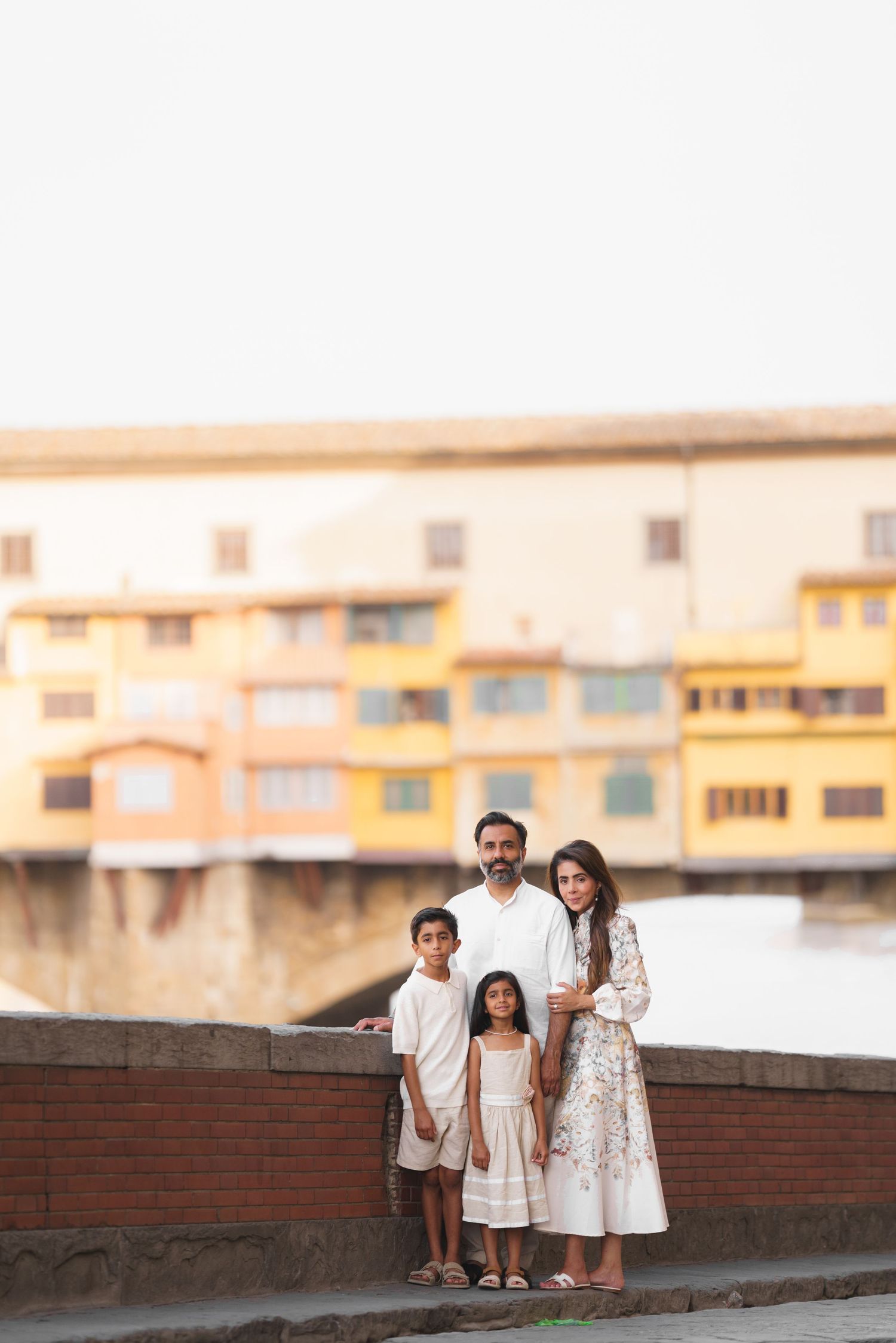Family of four posing in front of Ponte Vecchio bridge in Florence, Italy, wearing elegant white outfits.