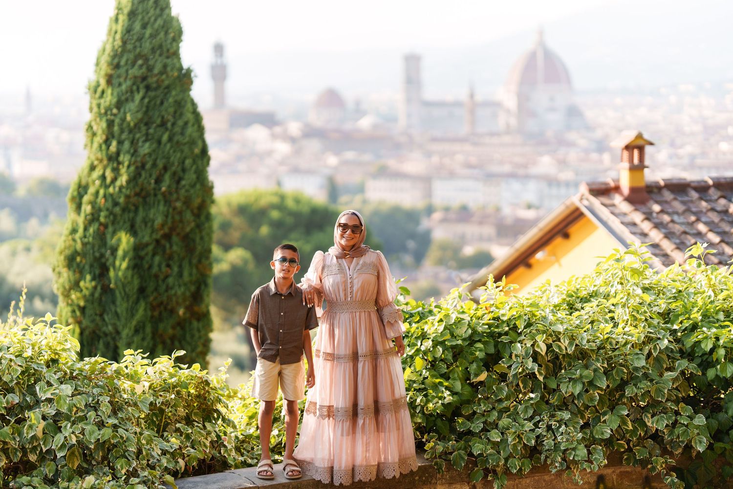Woman in pink dress and boy stand on a terrace overlooking Florence skyline with Duomo in background.