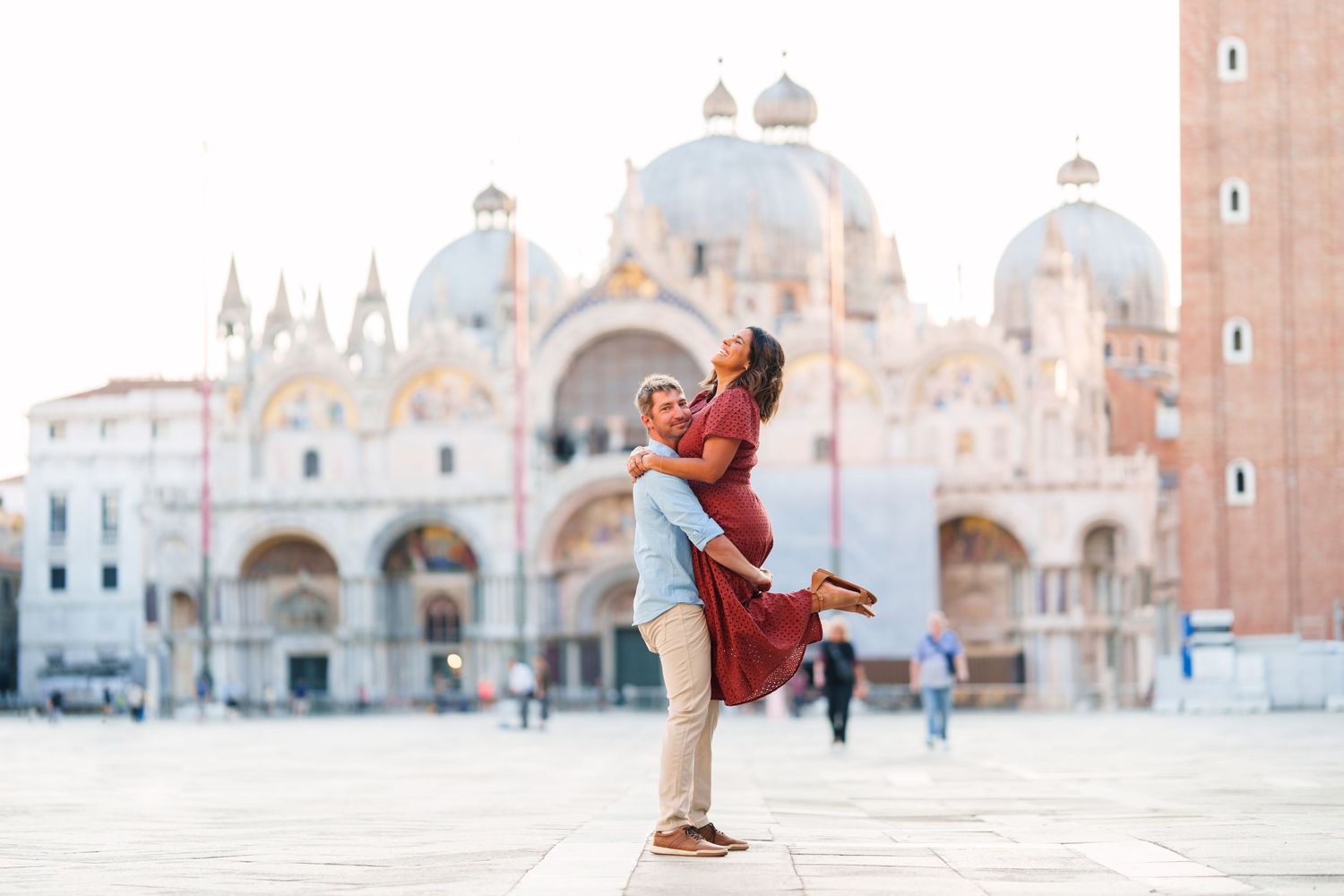 Couple embracing in St. Mark's Square, Venice, with the iconic Basilica di San Marco in the background.