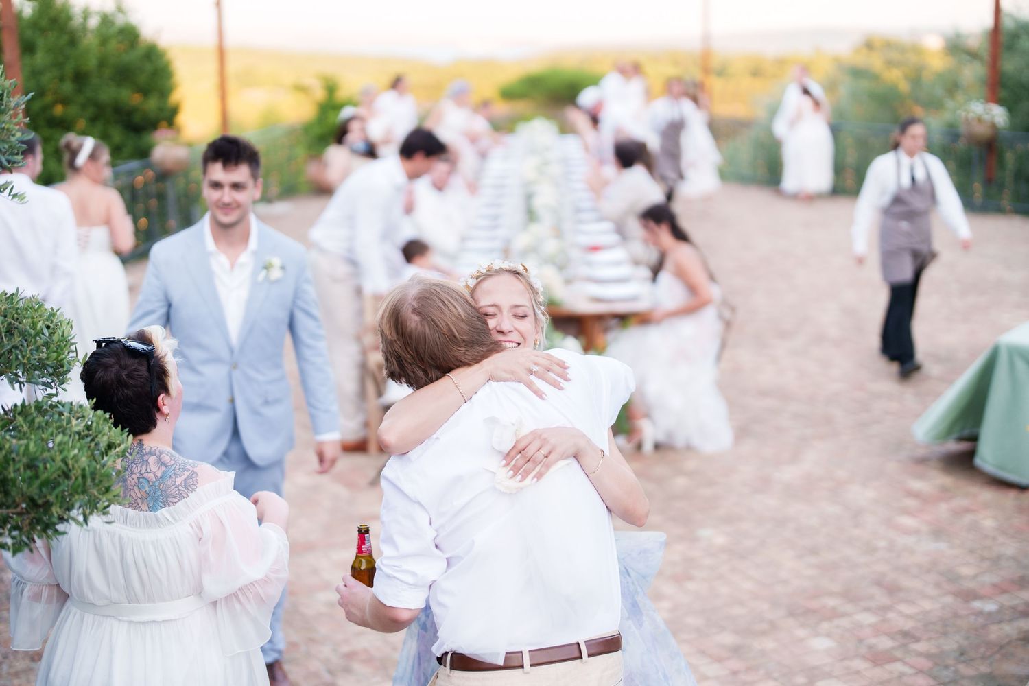 Guests in white attire hugging and celebrating at an elegant outdoor wedding reception with a decorated table.