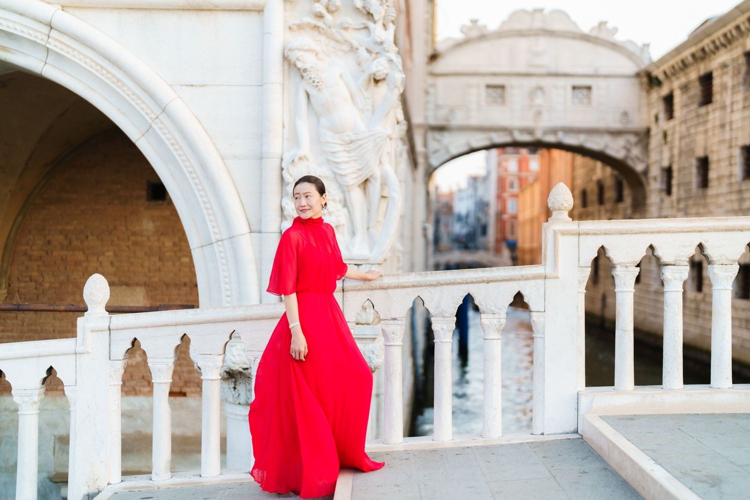 Woman in red gown posing near Bridge of Sighs in Venice, Italy.