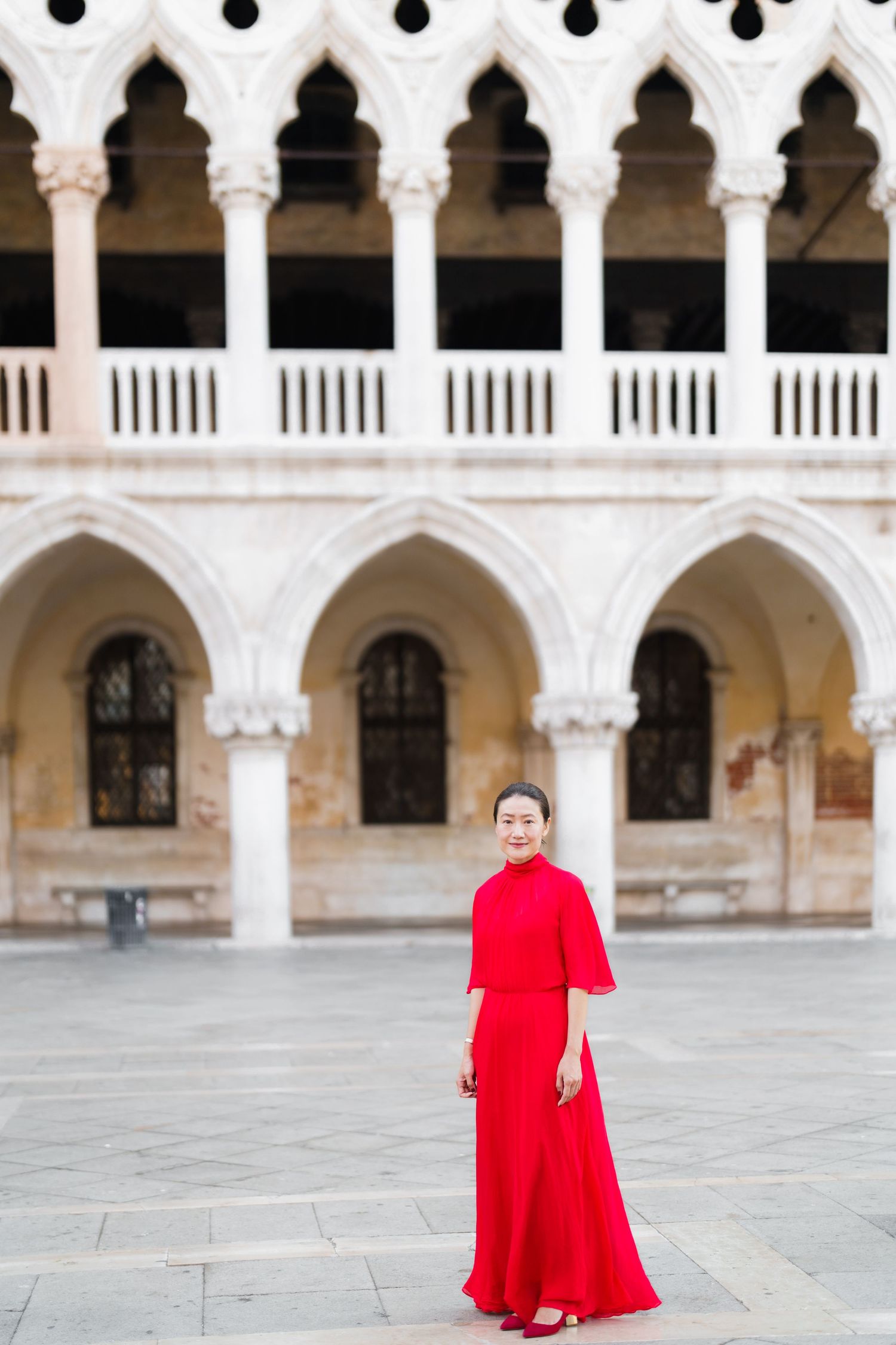 Woman in red gown poses before the ornate arches of Doge's Palace in Venice, Italy.