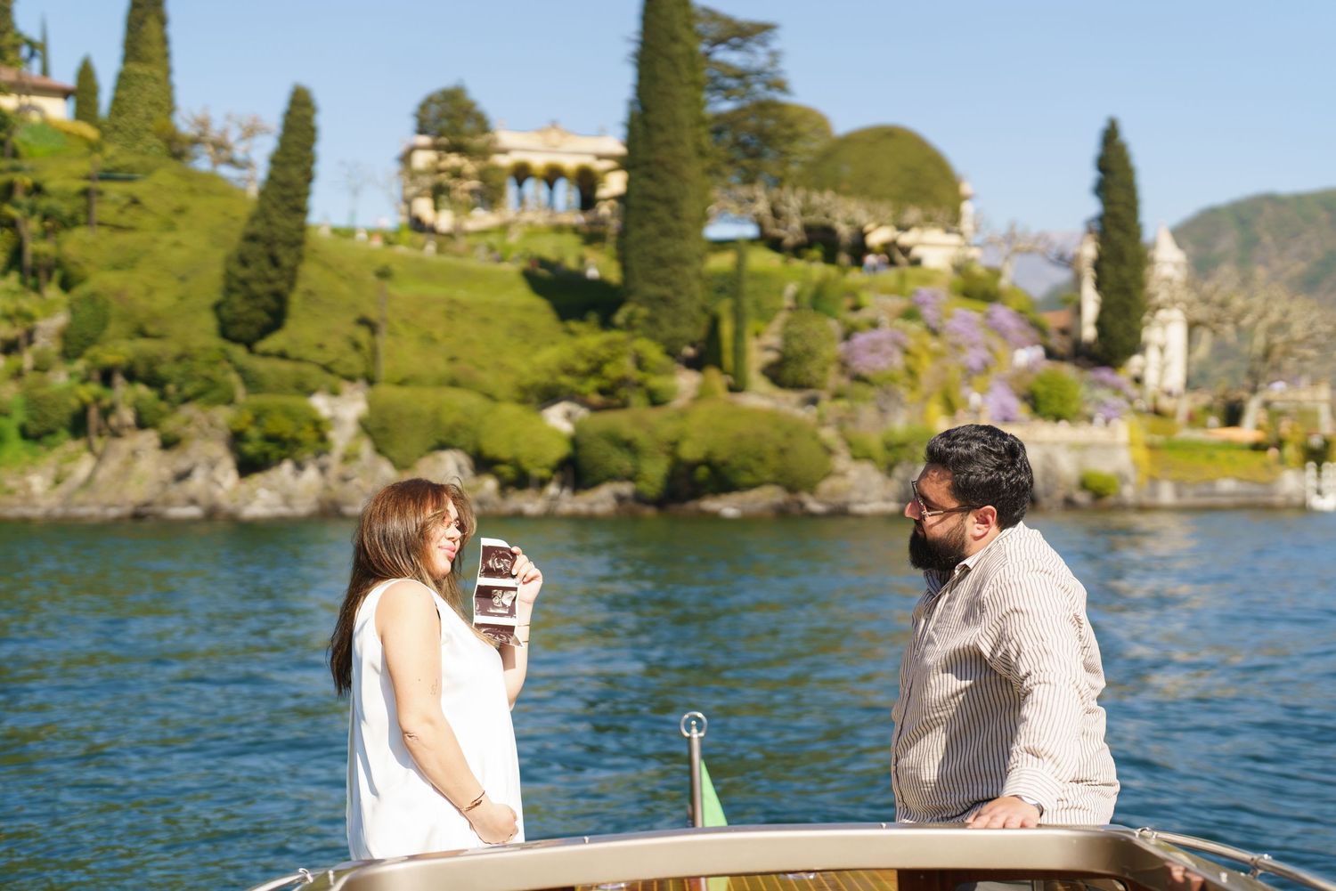 Couple enjoying a romantic boat ride on Lake Como with lush gardens and historic villa in the background.
