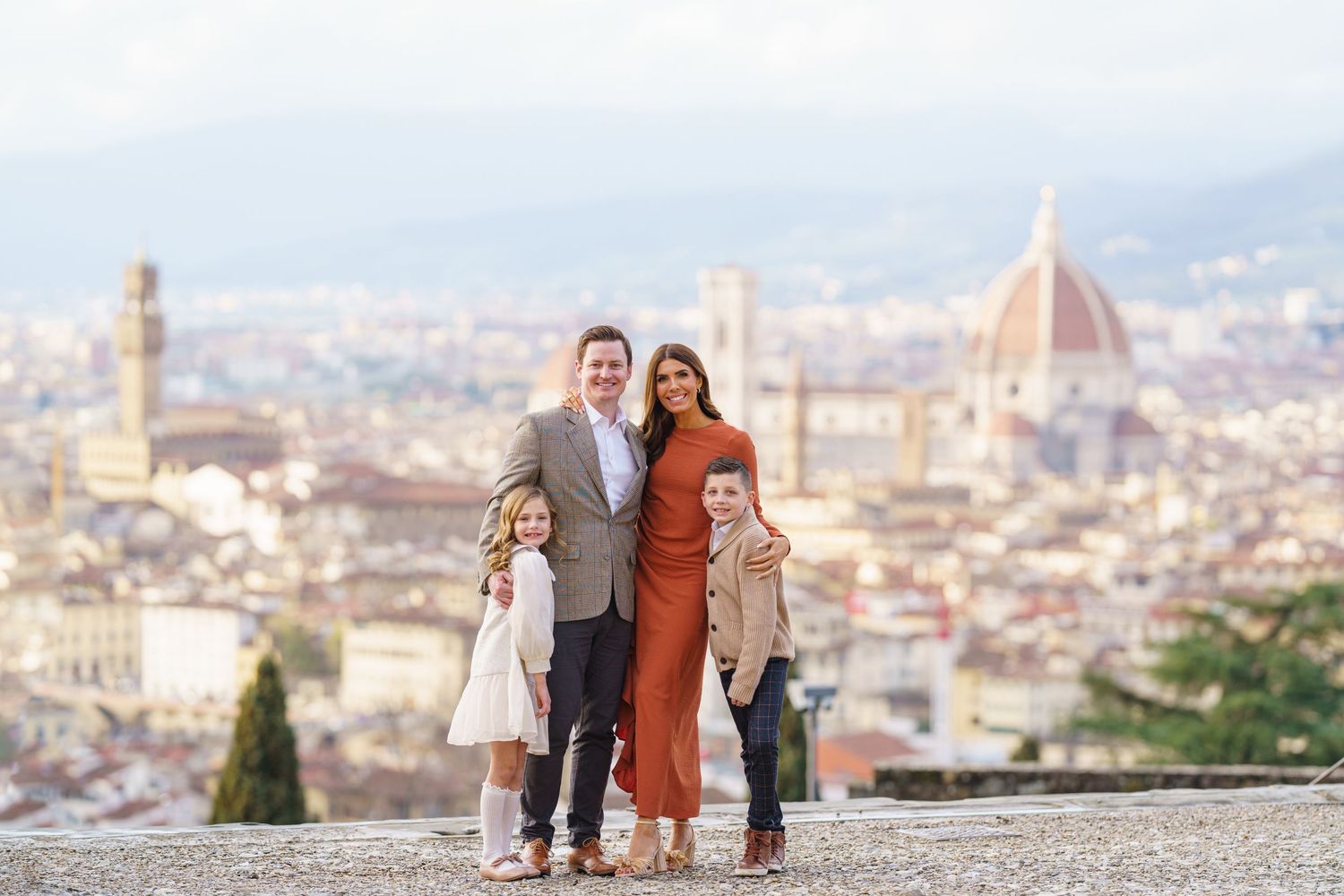 Family of four posing with Florence skyline and Duomo cathedral backdrop on a sunny day in Italy.