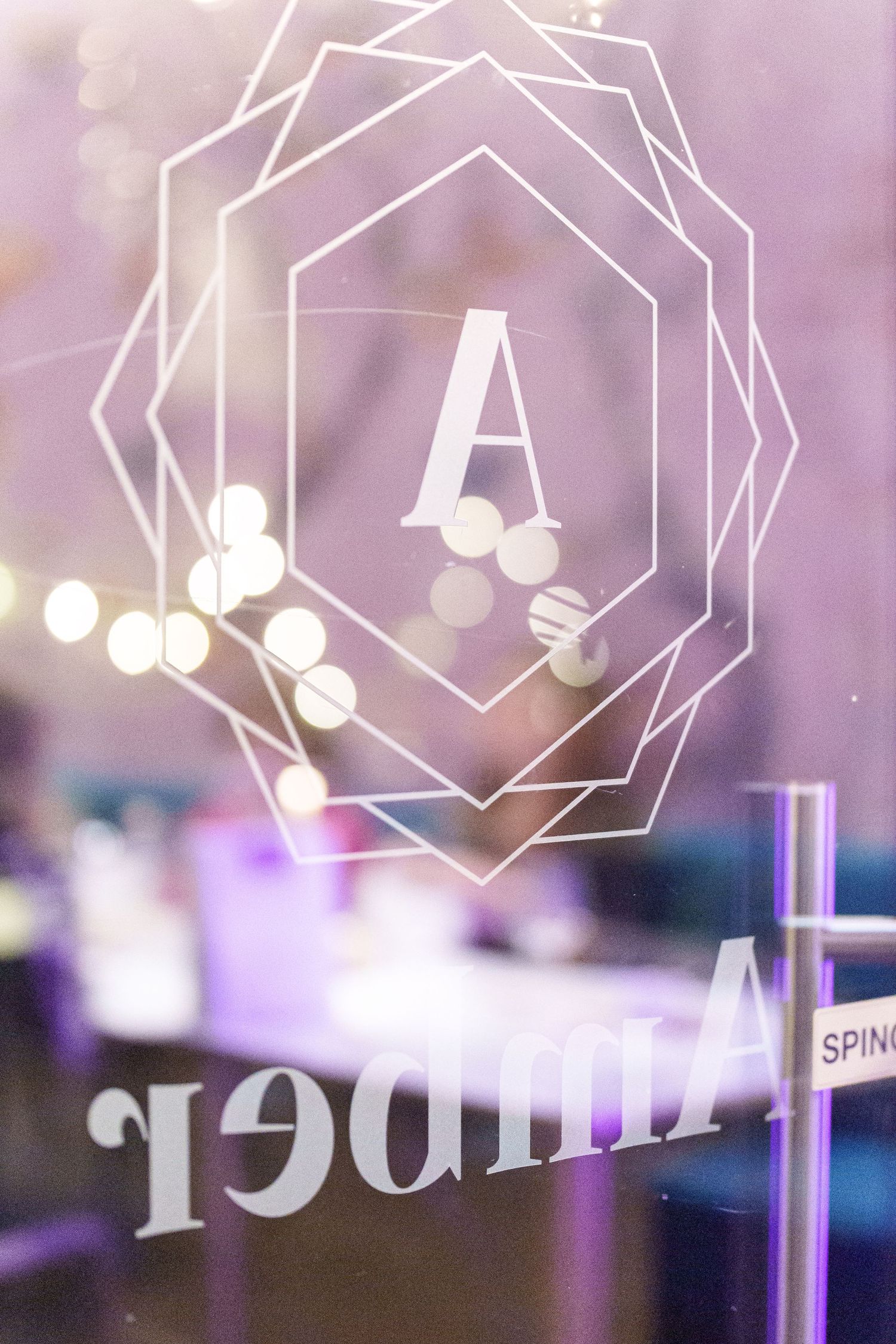 Elegant glass door with white geometric monogram letter A design and mirrored Amber text in soft purple lighting.