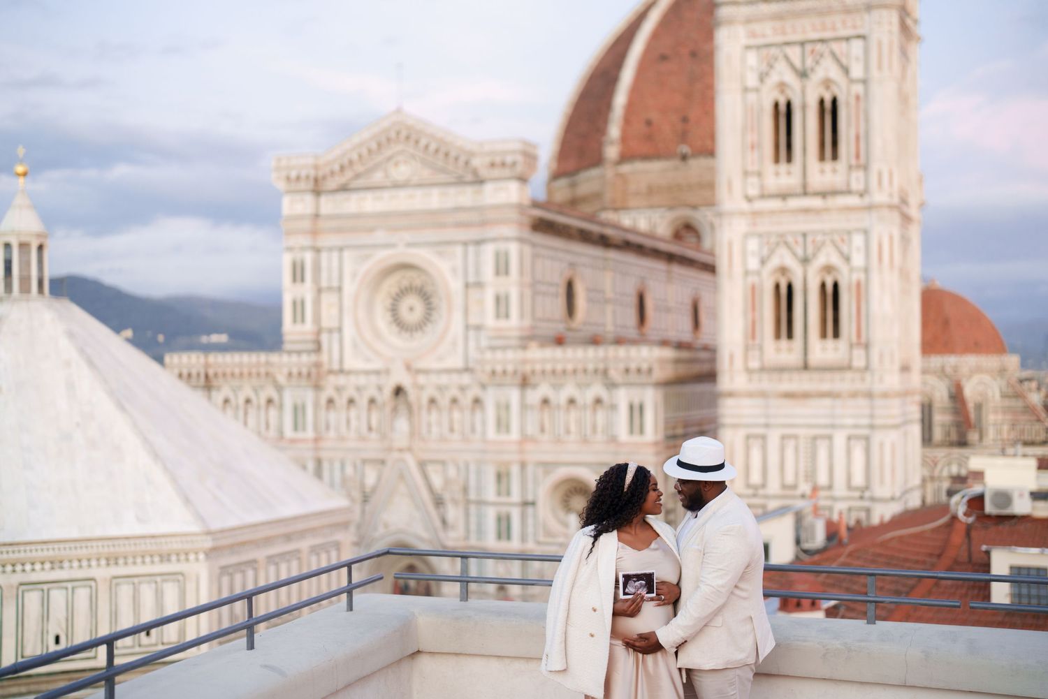 Couple embracing on a rooftop terrace with the Florence Cathedral dome and Giotto's Campanile in the background.