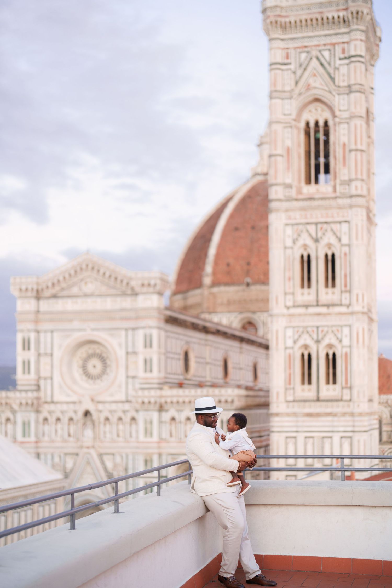 Father holding child on rooftop terrace with Florence Cathedral dome and Giotto's Campanile in background.