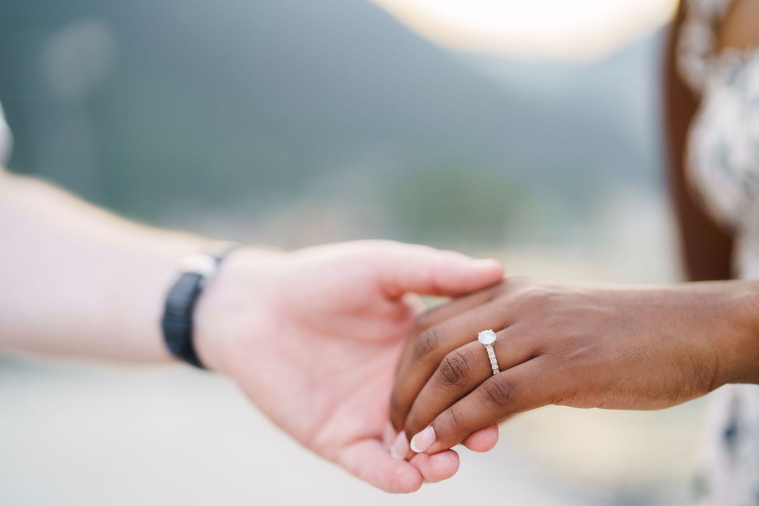 Close-up of interracial couple holding hands displaying a diamond engagement ring.