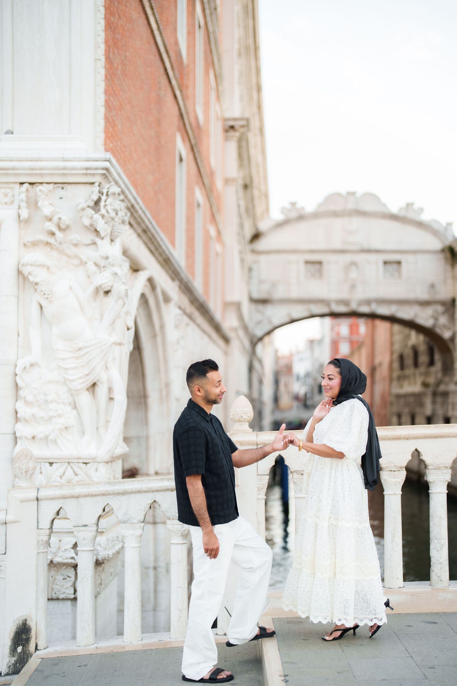 Couple in white and black outfits holding hands near the Bridge of Sighs in Venice, Italy.