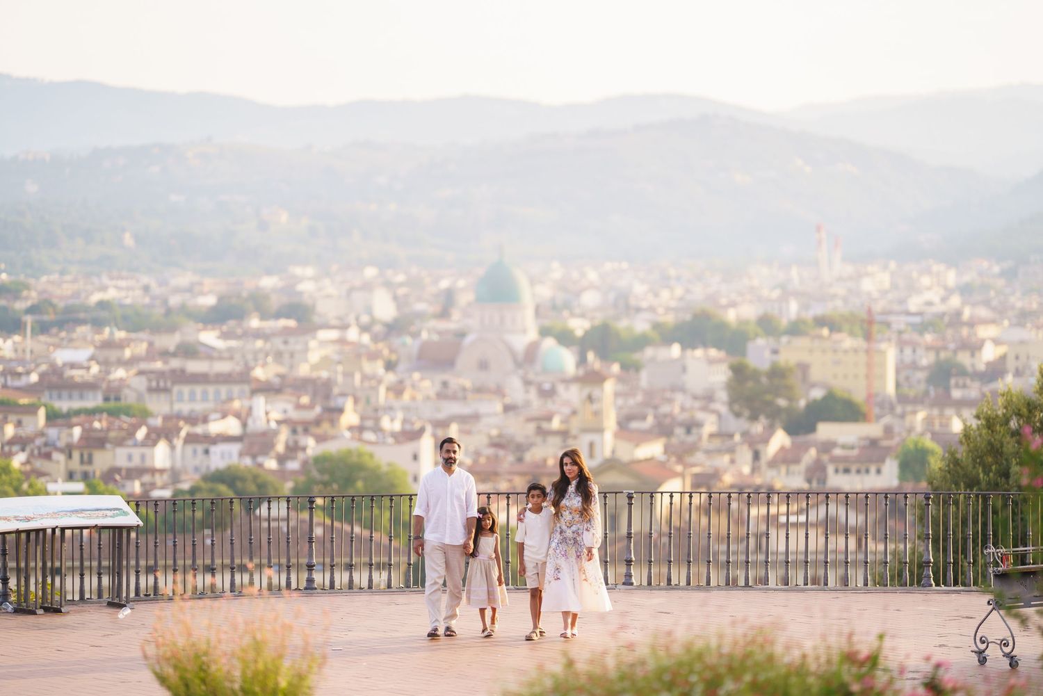 Family of three walking on a scenic overlook with Florence cityscape and rolling hills in the background.