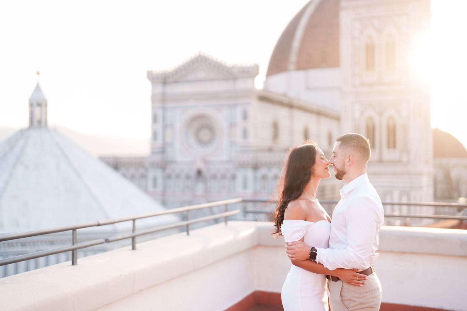 A couple embraces on a scenic rooftop terrace in Venice with golden sunlight and historic architecture in the background.
