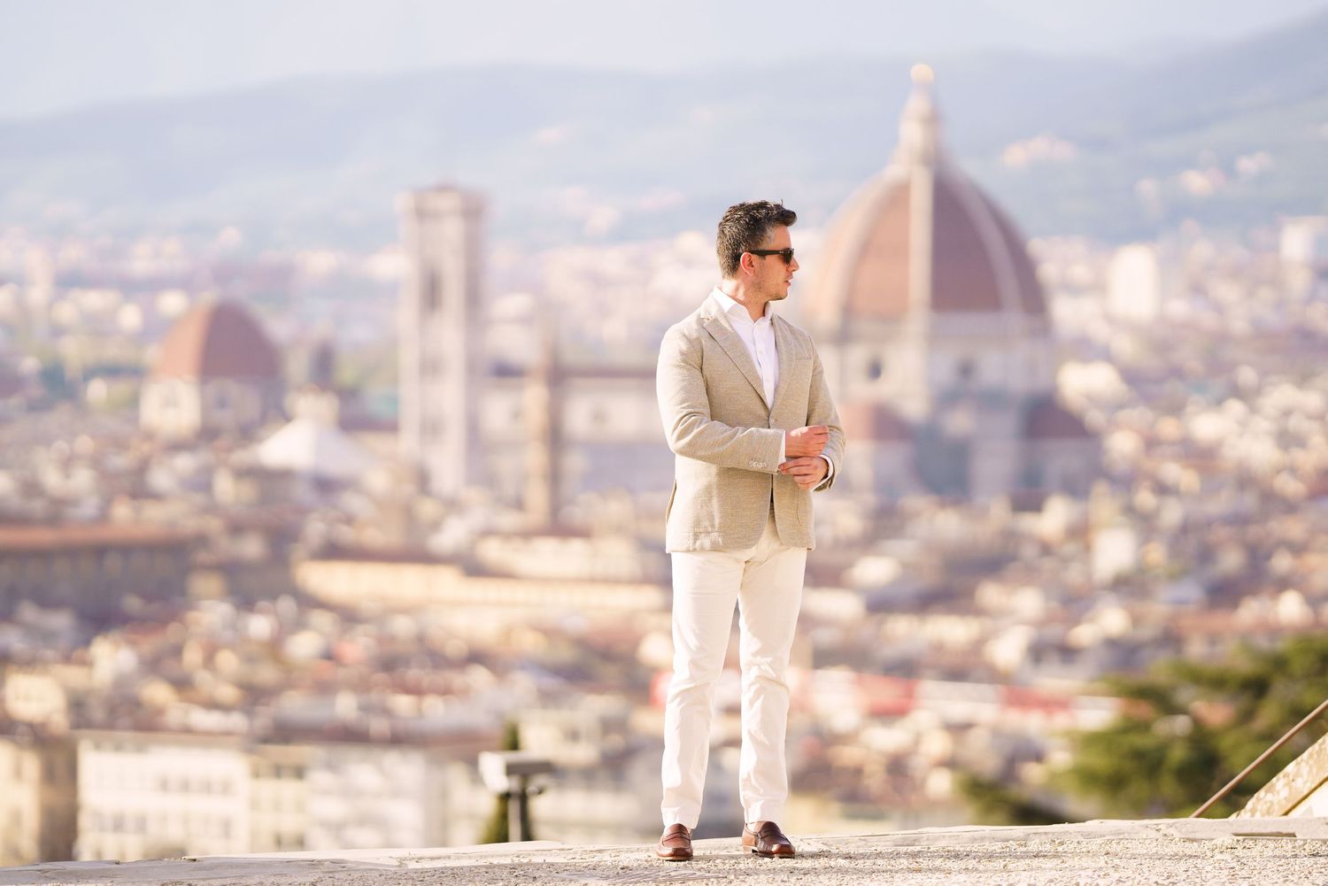 A romantic couple in light-colored outfits poses against the scenic backdrop of Florence, Italy with the Duomo visible.