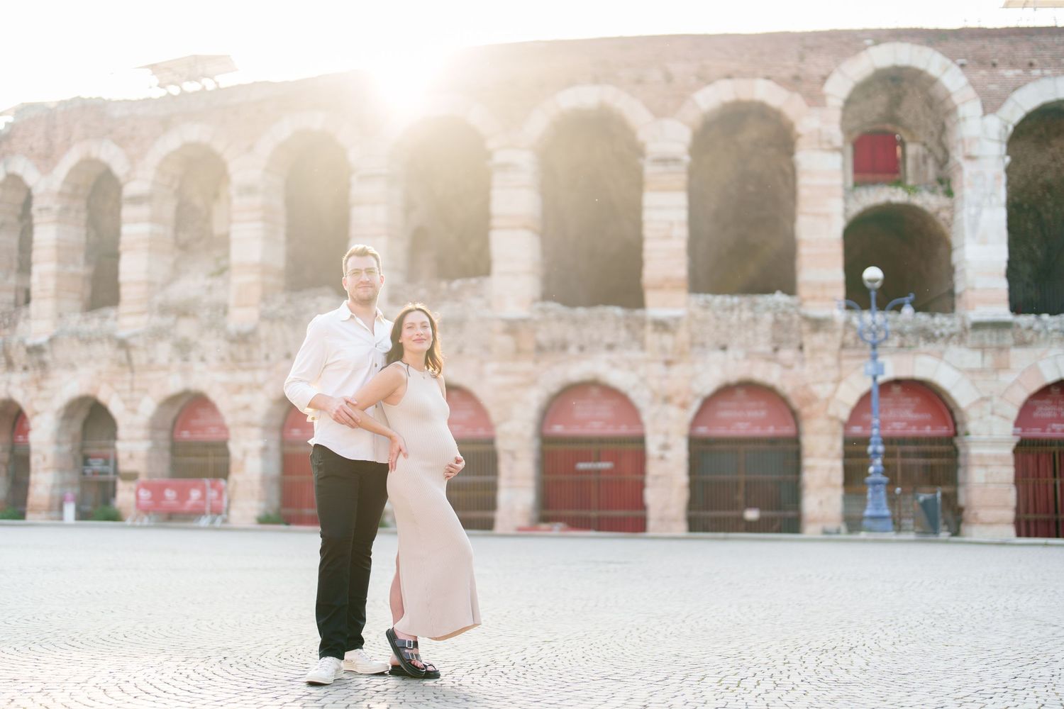 A romantic couple poses for photos under stone archways of a rustic outdoor venue at sunset.