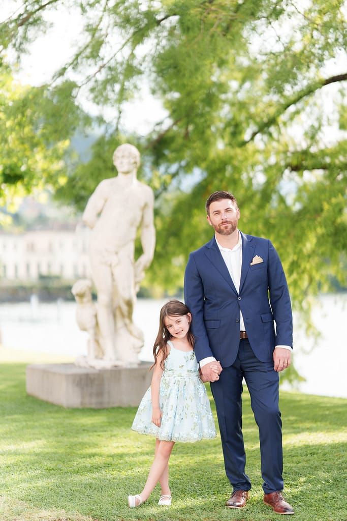 Father and daughter share a sweet moment together in a park setting with green trees in the background.