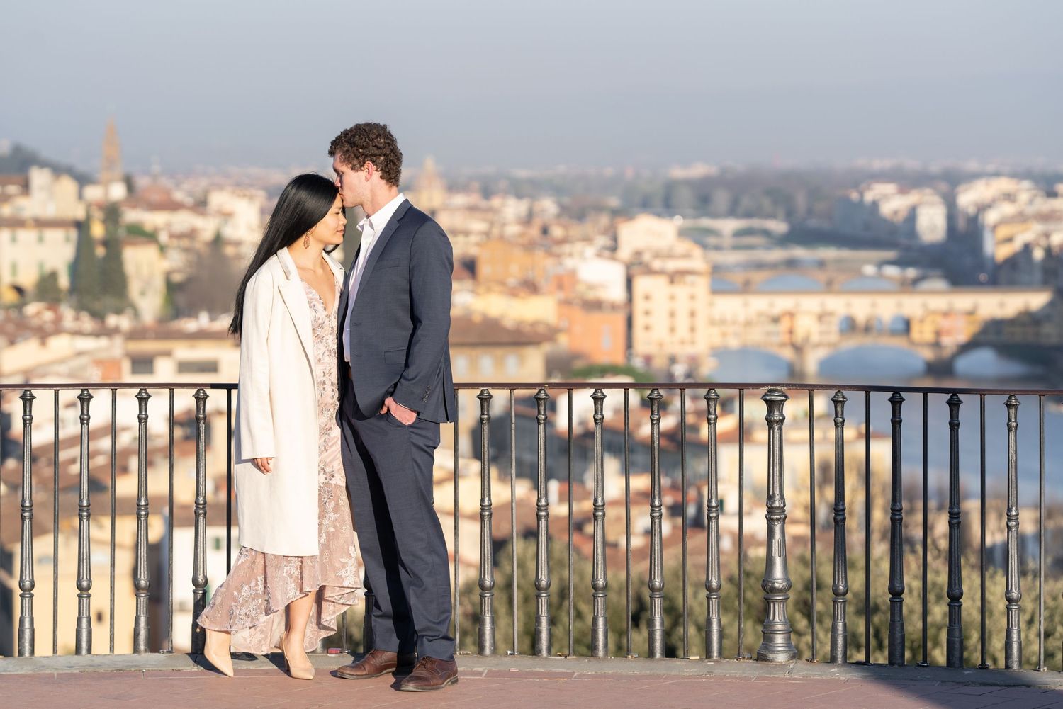 A couple shares a romantic moment at a scenic overlook with a beautiful cityscape view in the background.