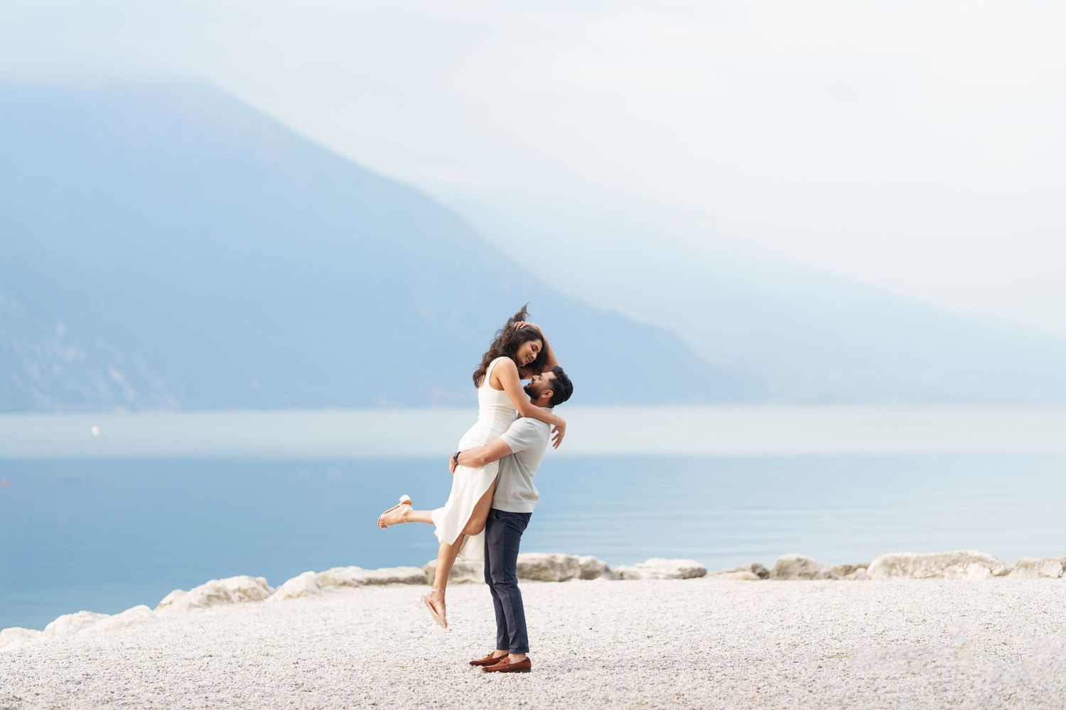 Couple embraces on a scenic beach with mountains and ocean in the background during a romantic photoshoot.