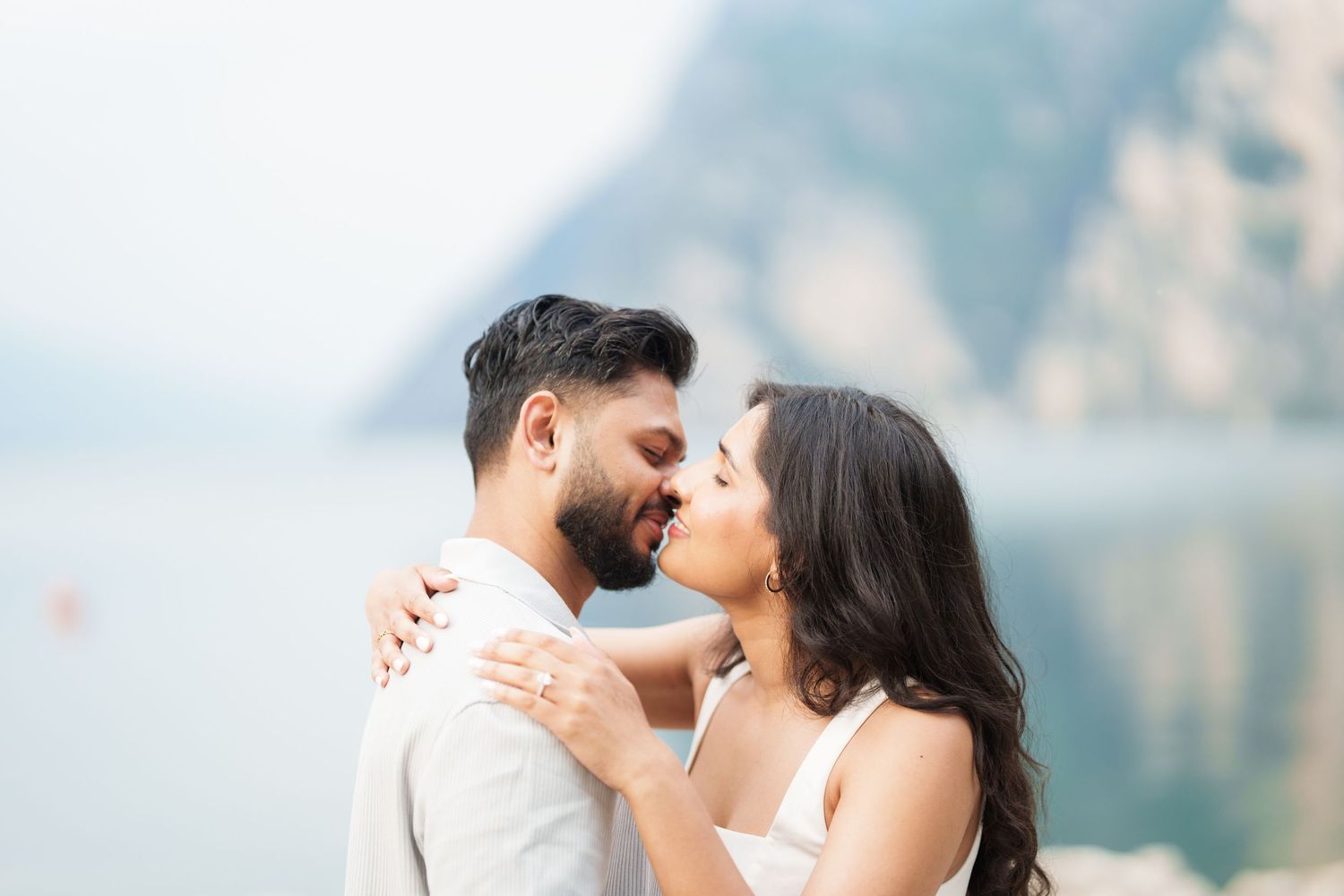 A romantic couple embraces while sharing an intimate moment against a misty mountain lake backdrop.