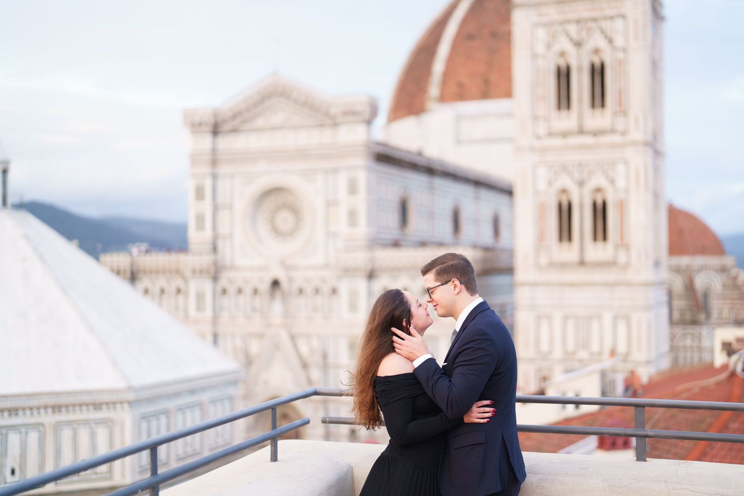 A couple embraces romantically against the backdrop of Florence's historic Duomo cathedral and cityscape at sunset.