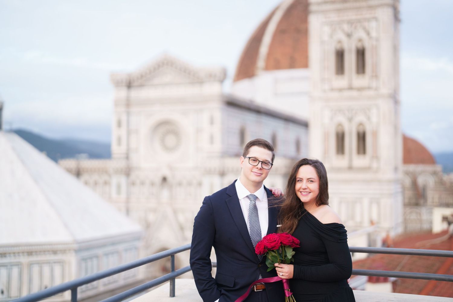 A couple stands on a terrace overlooking the Florence Cathedral and Duomo in Italy, with red roses.