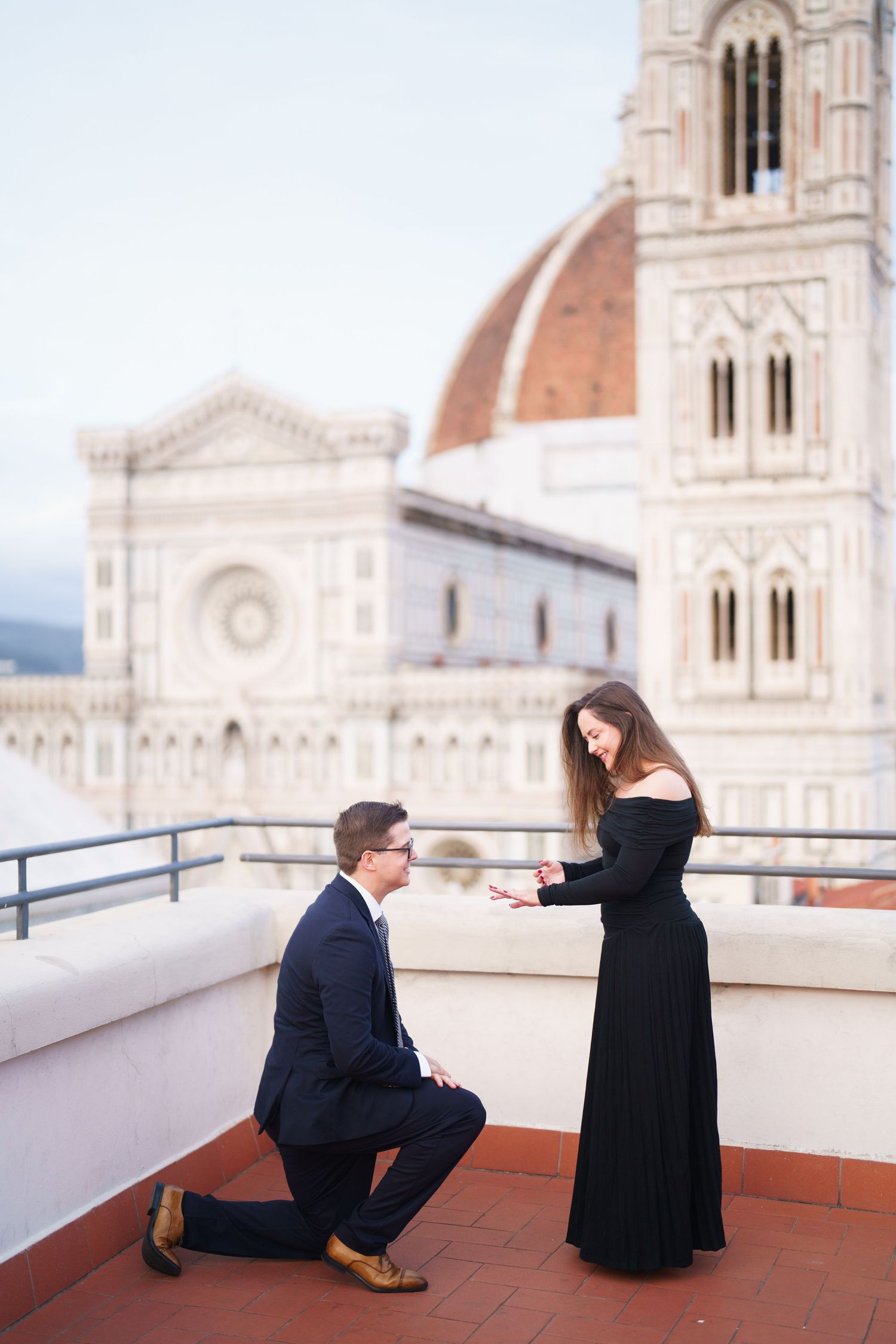Two figures in dark clothing sit and interact on a terrace overlooking Florence Cathedral's iconic dome in Italy.
