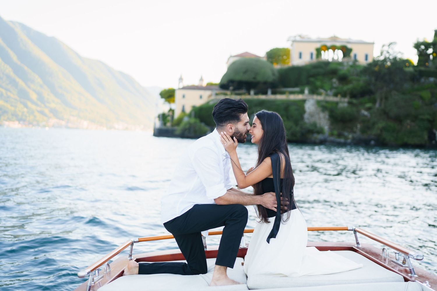 Romantic couple shares tender moment on wooden dock by tranquil lake during golden hour.