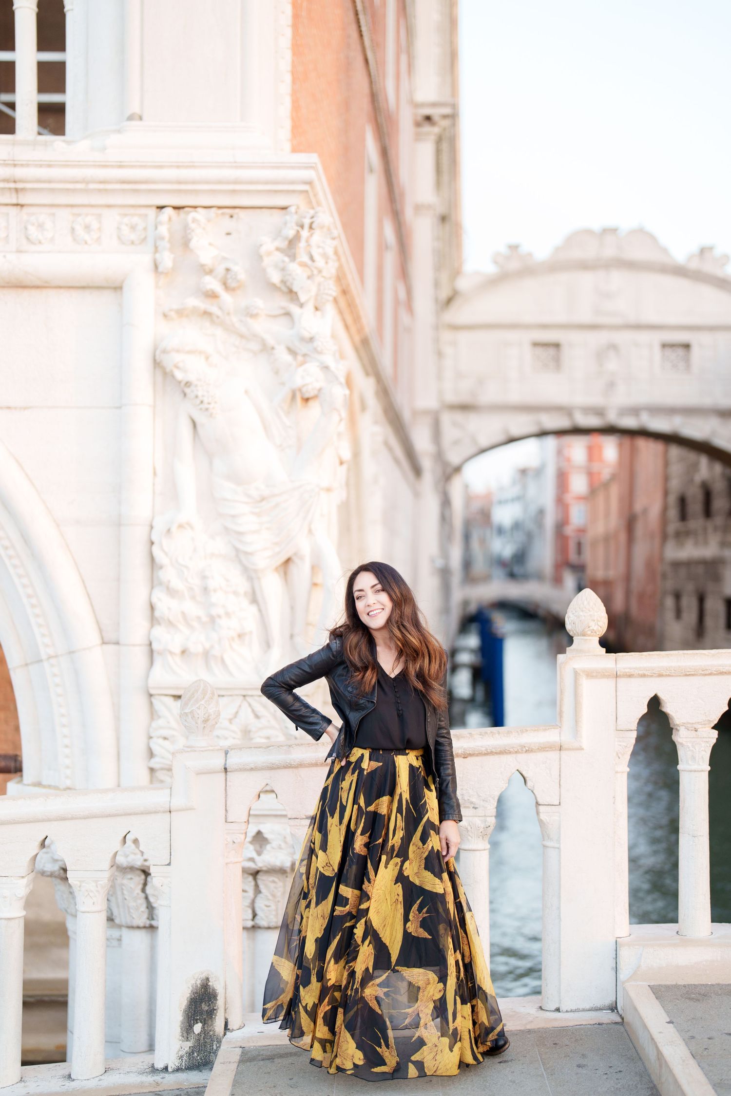 photographer veniceA person in a flowing black and gold dress poses elegantly against ornate white stone architecture in Venice.