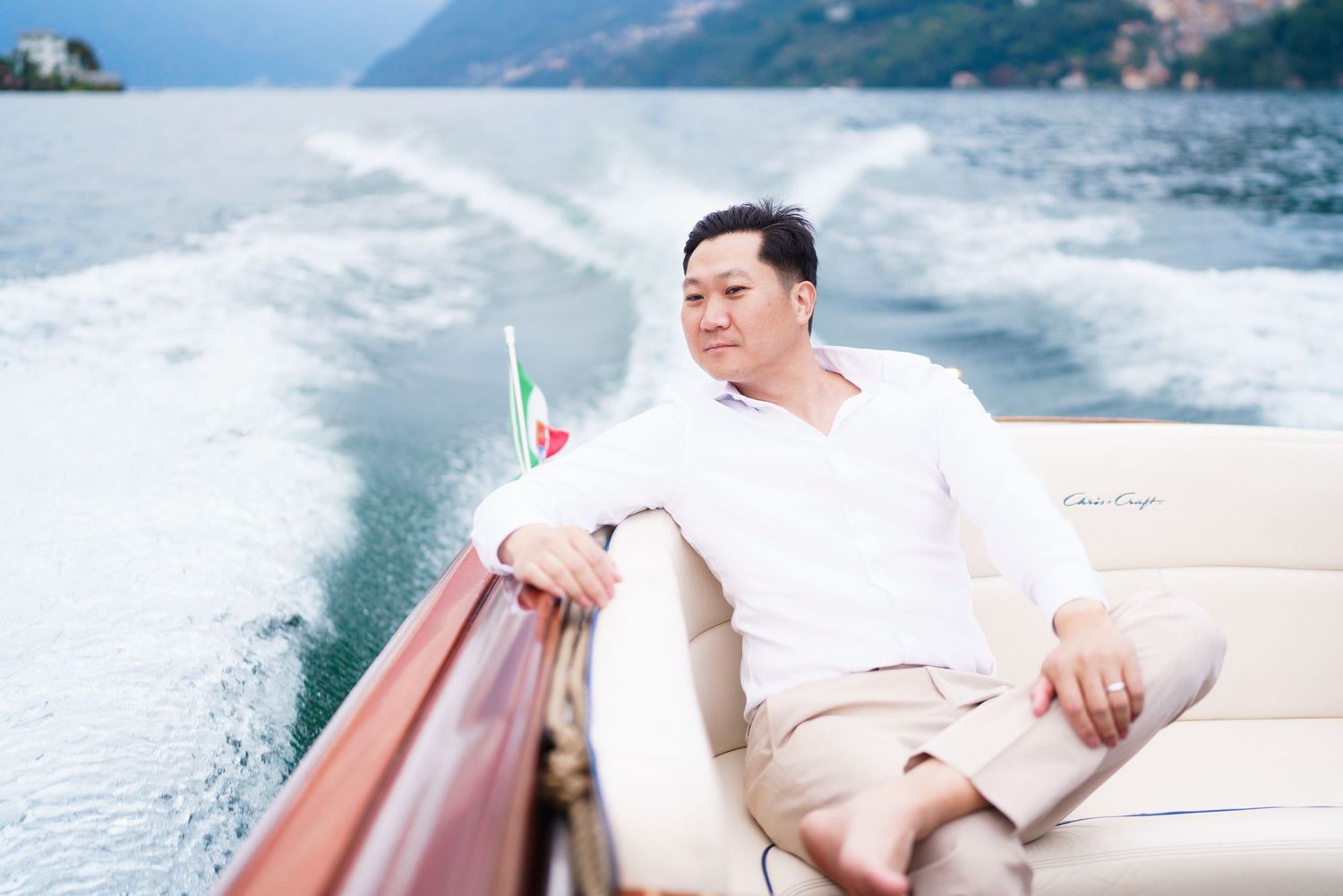 Someone relaxes on a cushioned boat seat while cruising across blue waters with mountains visible in the background.