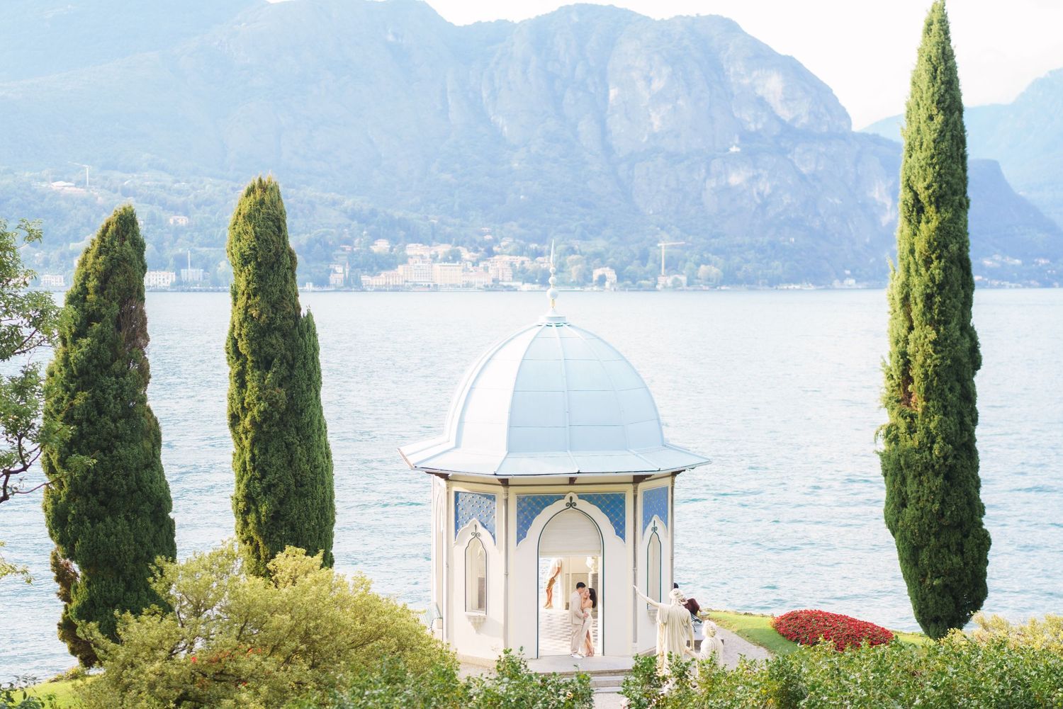 White domed gazebo overlooking Lake Como with tall cypress trees and mountains in the background.