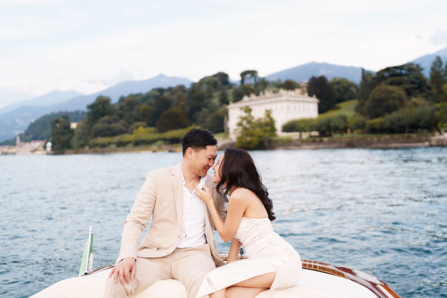 Romantic couple shares intimate moments during sunset photoshoot on boat at lake with mountains in background.