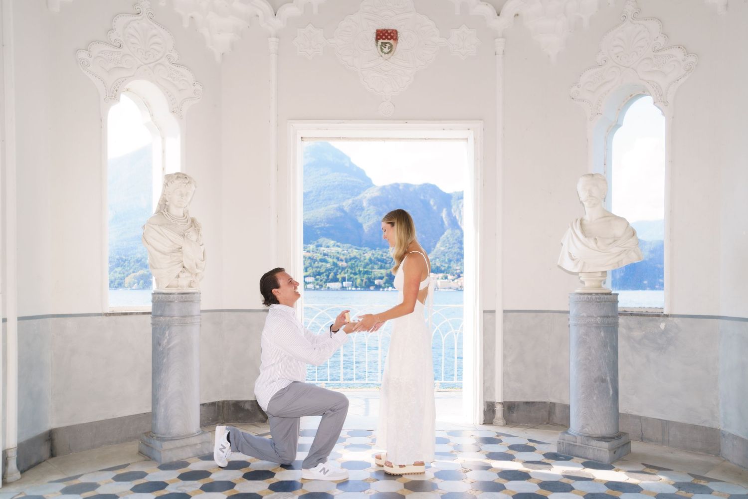 A romantic proposal moment in a white marble terrace overlooking scenic mountains and blue sky in the background.