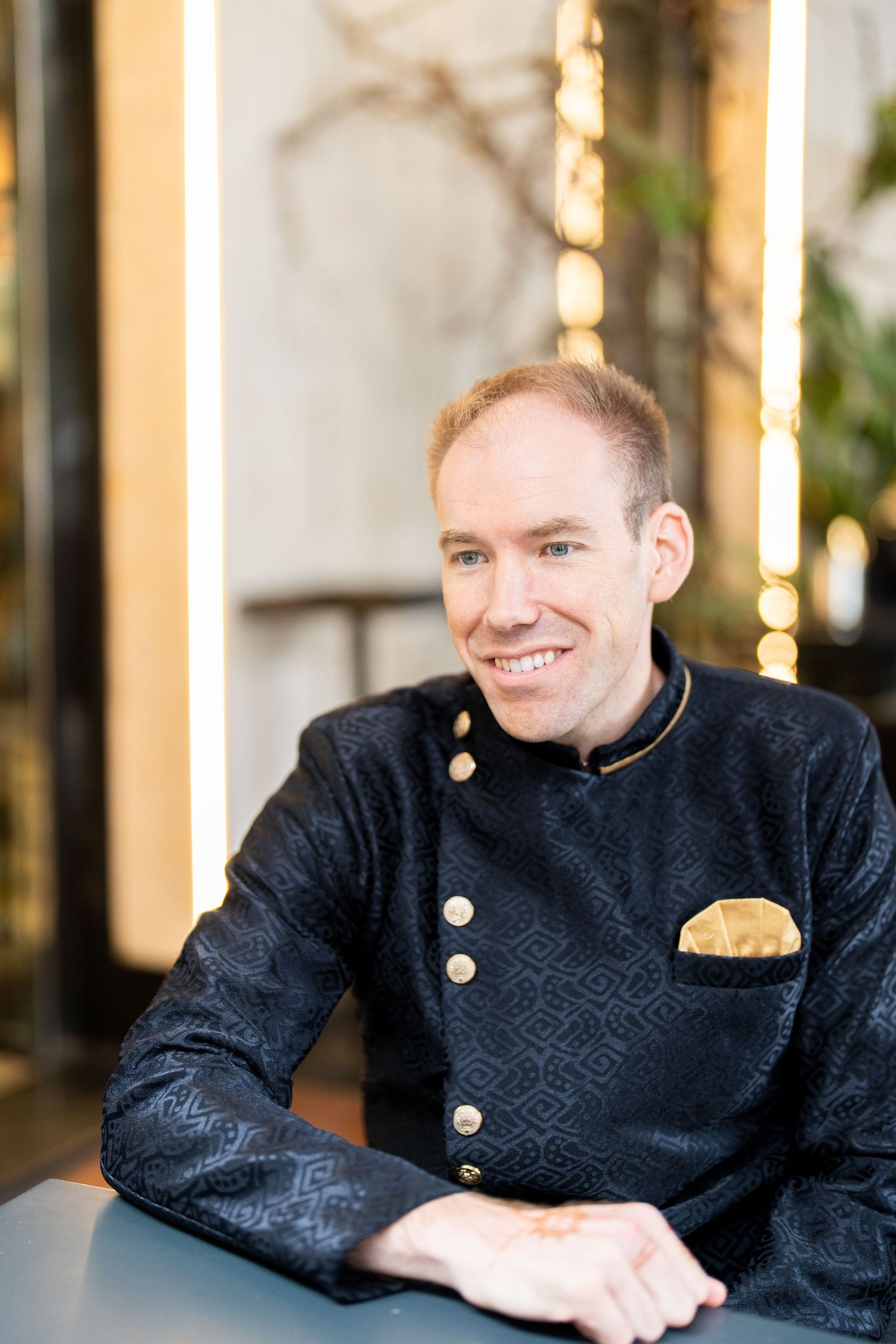 Portrait of person in formal black military-style jacket with gold buttons indoors.