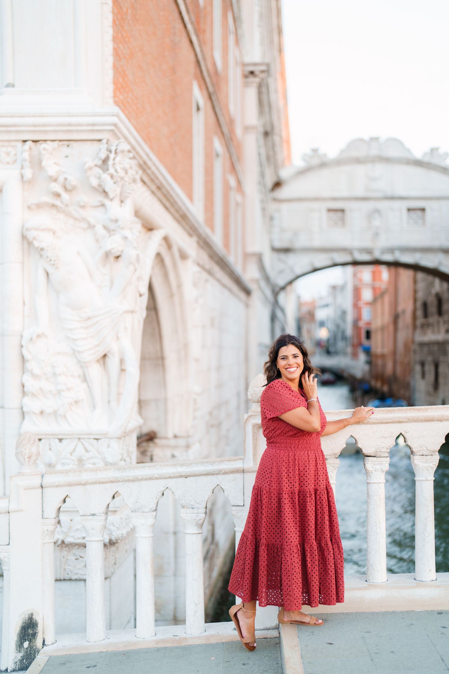 Woman in red dress standing by white balustrade near Bridge of Sighs canal in Venice, Italy.