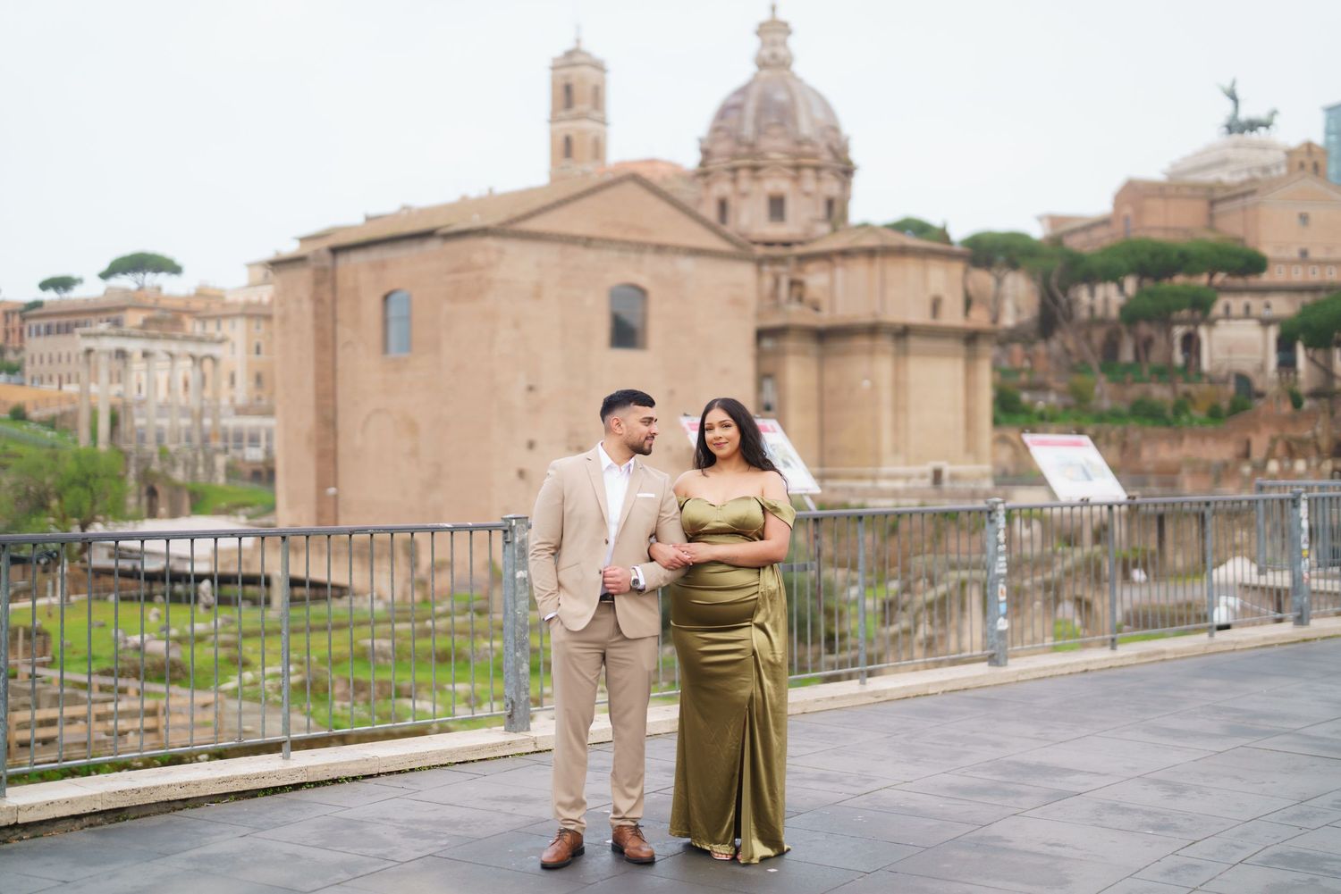 Couple posing in elegant formalwear with Rome's ancient Forum ruins and historic buildings in the background.