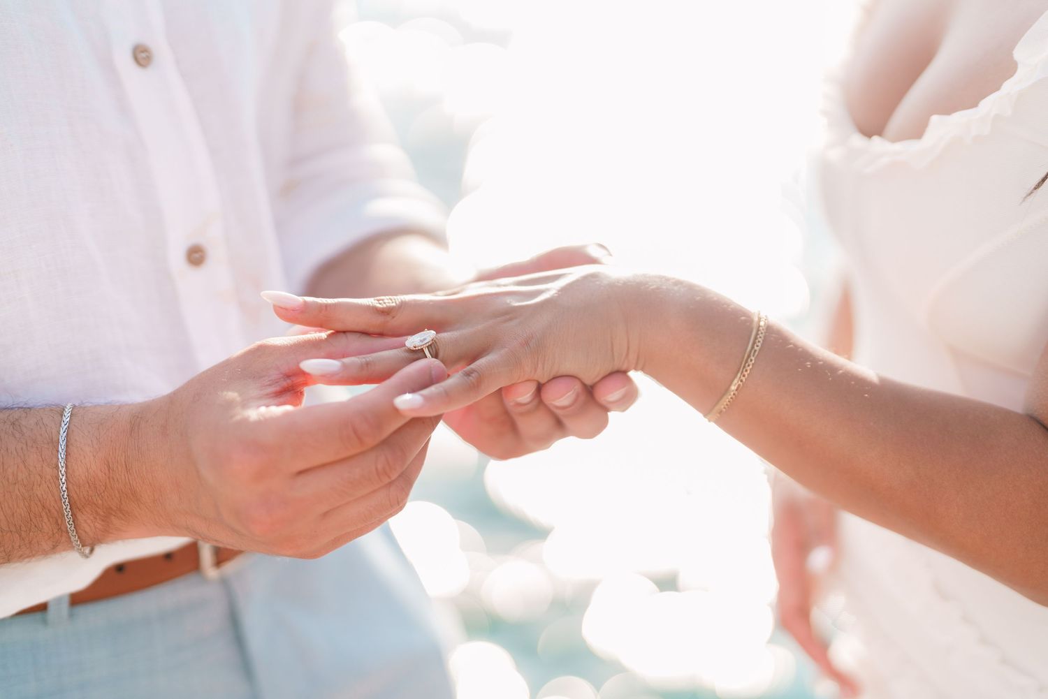 Close-up of groom placing wedding ring on bride's finger during outdoor beach ceremony.