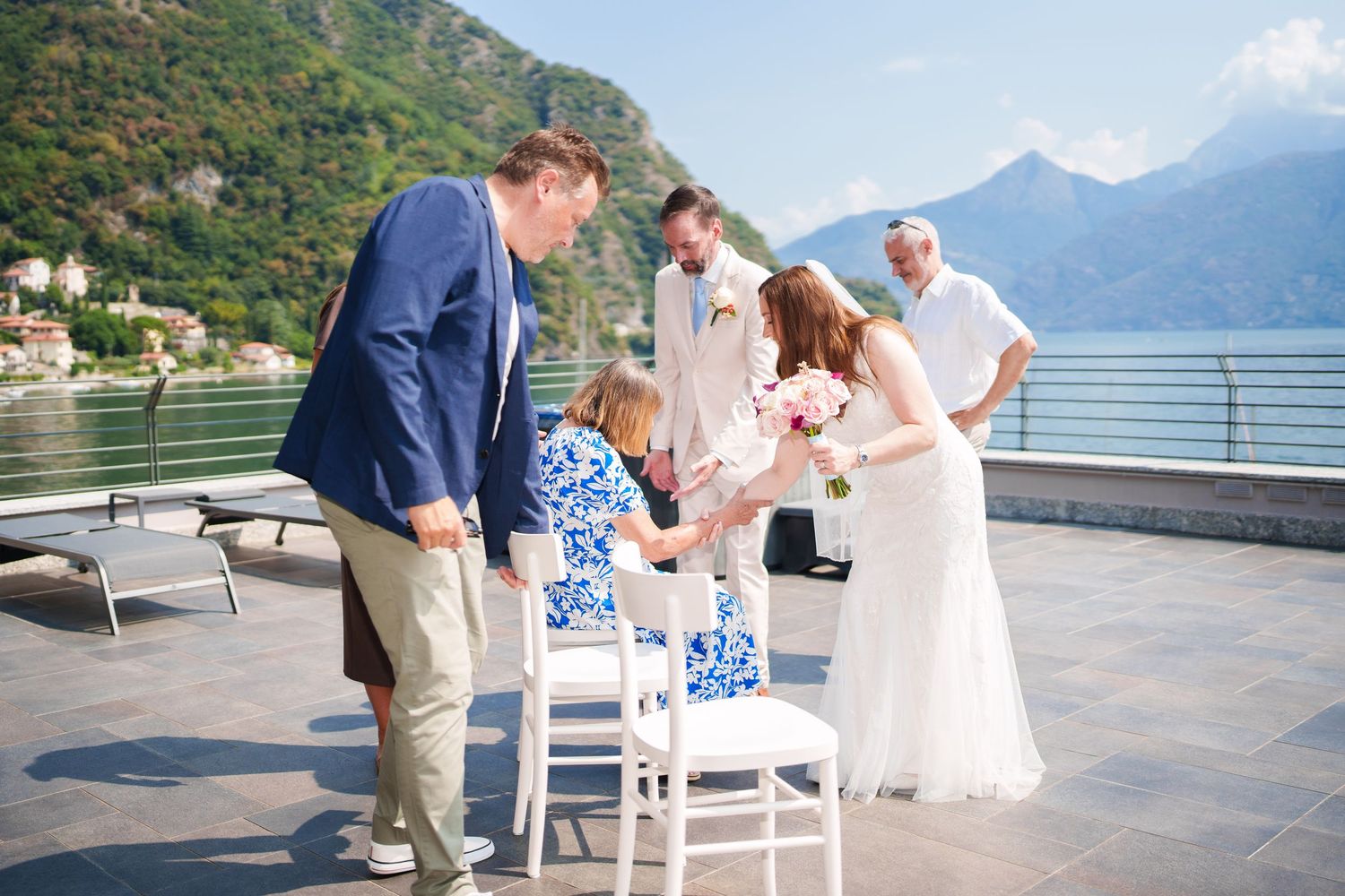Outdoor wedding ceremony on a lakeside terrace in Montenegro with bride, groom, and guests against mountain backdrop.