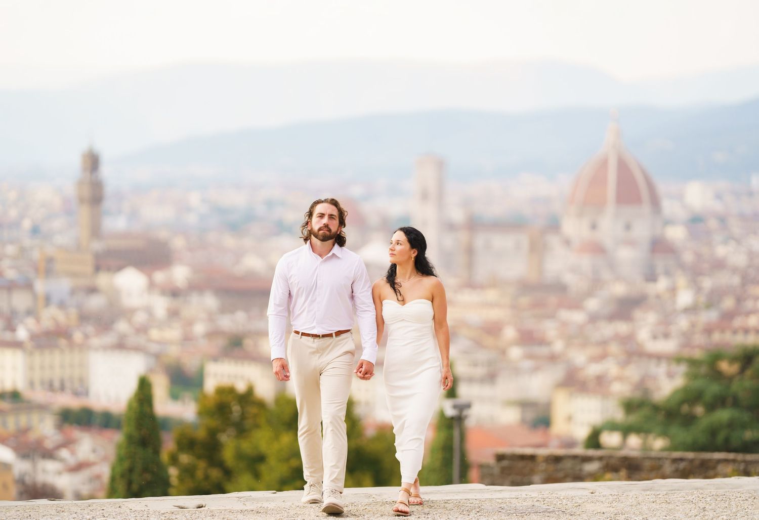 A couple walks hand in hand through Florence, Italy with the city's iconic Duomo cathedral and historic skyline in view.